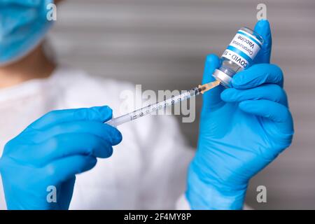 Close up of healthcare worker preparing a dose for injection of Covid-19 vaccine. She is wearing a medical mask and protective gloves and is holding a Stock Photo