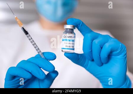 Close up of a healthcare worker wearing a medical mask and protective gloves holding a syringe and a glass vial of Covid-19 vaccine. Coronavirus vacci Stock Photo