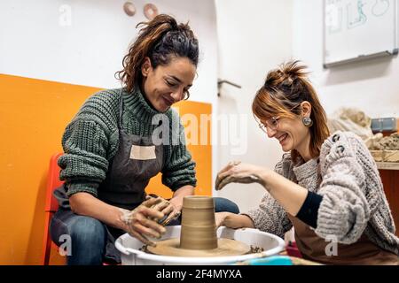 Stock photo of pottery teacher explaining to happy woman how to use spinning wheel. Stock Photo