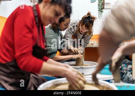 Stock photo of pottery teacher explaining to concentrated woman how to use spinning wheel. Stock Photo