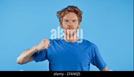 angry redhead man showing clenched fist isolated on blue Stock Photo