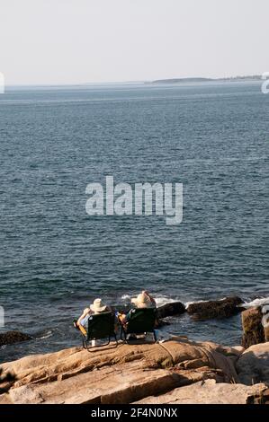 Two adults (unrecognizable) on vacation, relaxing in lawn chairs overlooking the ocean at Acadia National Park in Maine Stock Photo