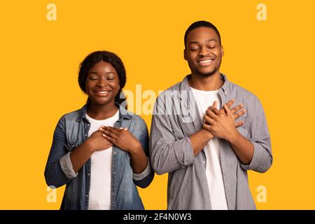 With Faith In Heart. Black couple praying with hands on chest Stock Photo