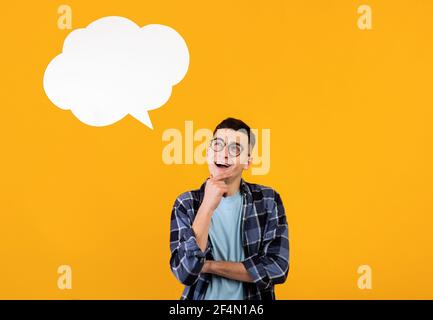 Thoughtful young guy looking at empty speech bubble over orange studio background, mockup for design Stock Photo