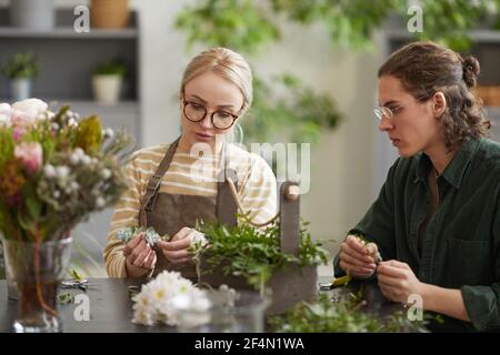 Portrait of female florist teaching young man while creating floral compositions in workshop, copy space Stock Photo