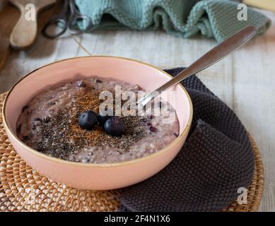 fresh cooked blueberry porridge with chia seeds and cinnymon served in a pink bowl with spoon isolated on wooden table Stock Photo