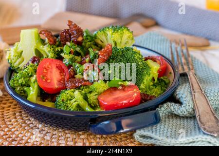 broccoli salad with fresh and dried tomatoes, garlic, red onions marinated in a balsamic vinegar and olive oil dressing served in a bowl
