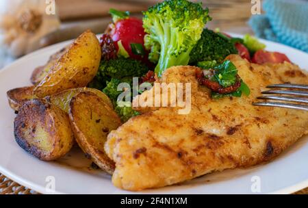 mediterranean fish dish with fried redfish fillet, roasted rosemary potatoes and a broccoli, tomato salad served on a plate. Closeup  and isolated Stock Photo