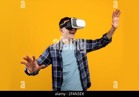 Joyful young guy using virtual reality headset, controlling cyber environment with moving gestures on orange background Stock Photo