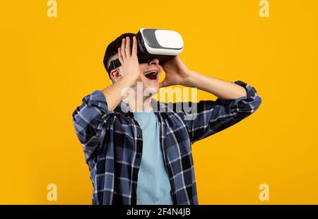 Cheerful young man in virtual reality glasses playing online game, feeling excited on orange studio background Stock Photo