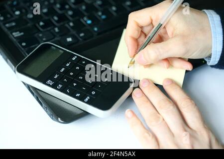 Closeup of a hand holding a pen over blank paper with calculator and laptop Stock Photo