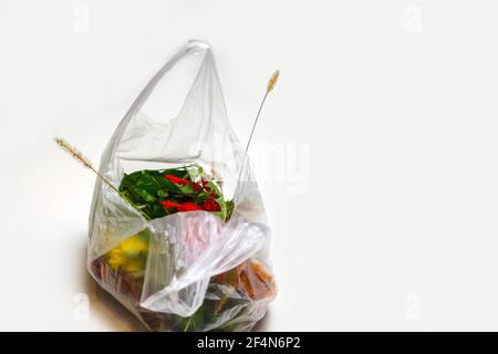 DEFOCUS. Ecological problem. Red and green plants flowers in a plastic bag on a white background. A dry blade of grass sticks out. Ecological problems Stock Photo