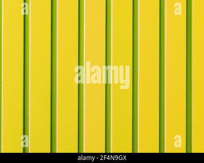Yellow metal fence made of corrugated steel sheet with vertical rails. Corrugated yellow with light green stripes iron sheet close up background. Stock Photo