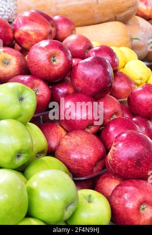 Bright picture of fresh red and green apples, lemons, pumpkins and other vegetables for sale in the market. Vertical image, close-up. Stock Photo