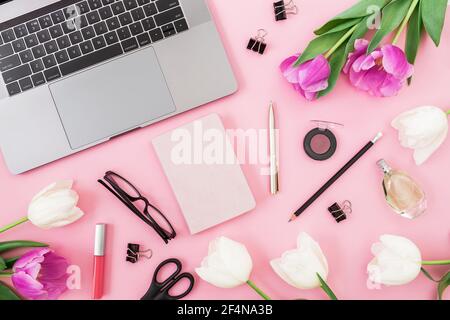 Laptop, tulips flowers, clipboard, glasses, pen and scissors on pink. Flat lay. Top view. Freelancer concept Stock Photo