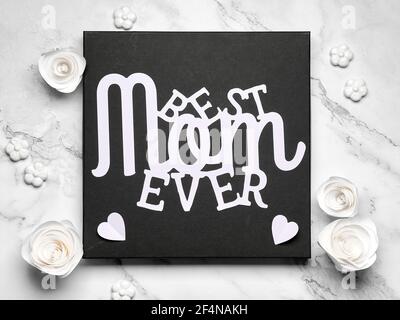 Paper text Best Mom Ever on black square board, frame. Greeting card design for Mother's day. White paper roses on ivory, off white marble background Stock Photo