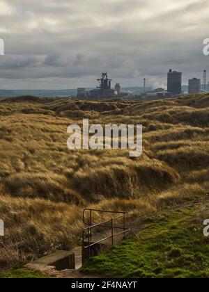 Nature in post-industrial landscape image showing a wide view from South Gare, across grass-covered, wind blown dunes to the derelict steel mill. Stock Photo