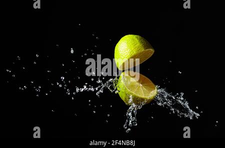 Juice splashes out of a cut lime on a black background. Stock Photo