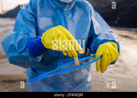 Gloved hands of contemporary researcher or ecologist in protective coveralls putting flask with sample of dirty water into packet Stock Photo