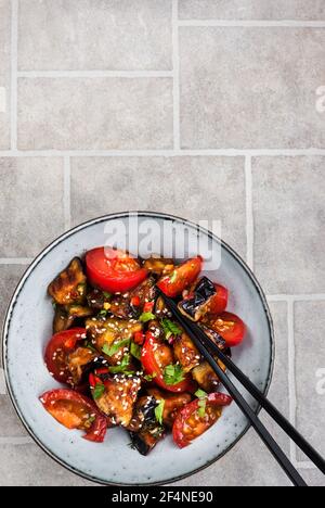 Close up of chinese style eggplant stir-fry with sesame, chili pepper and tomatoes, top view, copy space Stock Photo