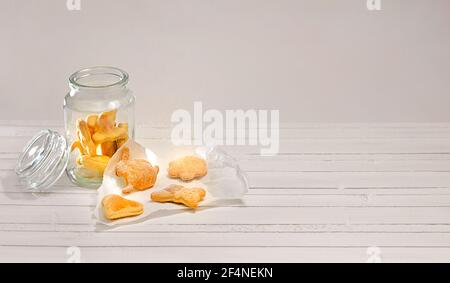 Glass jar with curly cookies sprinkled with powdered sugar. On a white wooden countertop. Stock Photo
