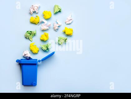 Blue recycle bin with crumpled colored paper balls on a blue background with copy space.Paper recycling concept Stock Photo