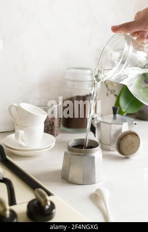 The process of making coffee in the home kitchen. Water is poured from a jug into a geyser coffee maker. Vertical orientation. Stock Photo