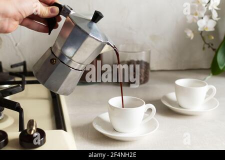 Coffee is poured from the geyser coffee maker into the espresso cup. The concept of making coffee at home. Horizontal orientation. Stock Photo