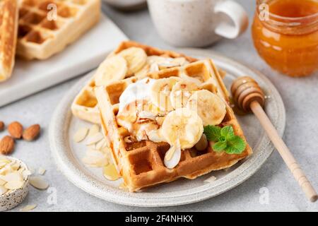 Sweet belgian waffles with banana, caramel and almonds. Dessert square shape waffles served with almond flakes, banana slices, caramel sauce and whipp Stock Photo