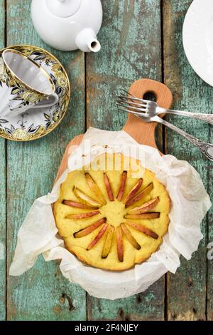Tea time. Homemade tasty round cake with apples freshly baked in paper with teaware on robin egg blue background above view Stock Photo