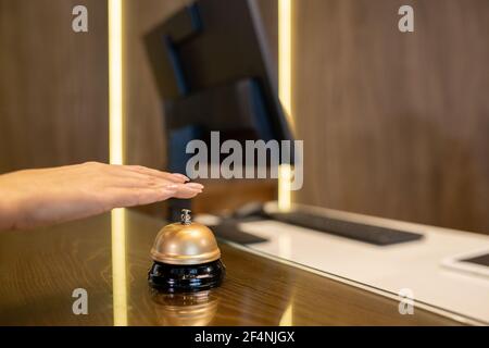 Hand of young woman over bell on wooden reception counter going to push button and call for receptionist to registrate her in hotel room Stock Photo