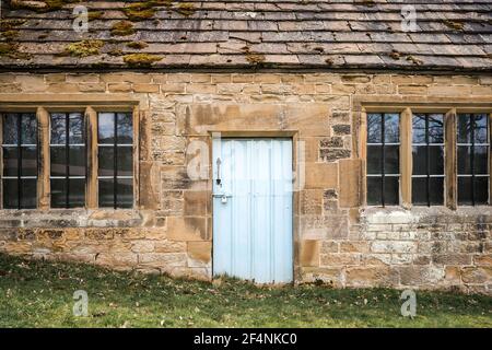Blue door in abandoned old cottage left empty in woodland forest.  Stone walls and lead glass windows. Entrance lock handle to deserted traditional Stock Photo