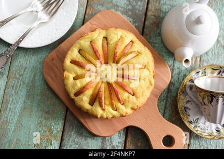 Homemade delicious rustic cake with apple slices looking like sun rays with teaware on shabby wooden blue table above view Stock Photo