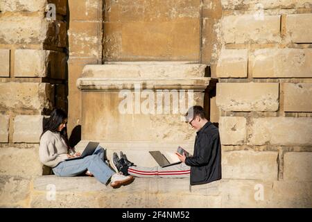 Oxford, UK 22 Nov 2020: Two students sitting in the sun on Ratcliffe Camera wall slope using laptops for learning. Young girl and boy research informa Stock Photo