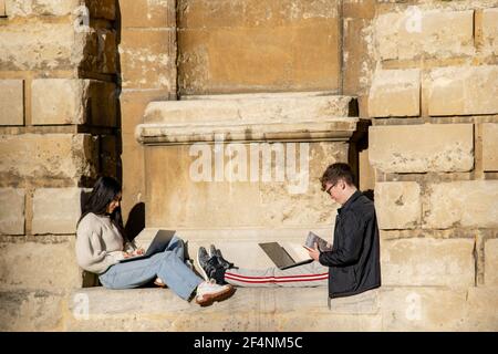 Oxford, UK 22 Nov 2020: Two students sitting in the sun on Ratcliffe Camera wall slope using laptops for learning. Young girl and boy research informa Stock Photo