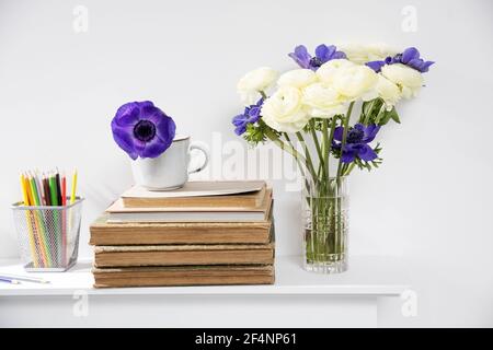 One blue anemone in a cup in the style of the seventies on the table with books as an interior decoration. Pencil holders with pencils Stock Photo