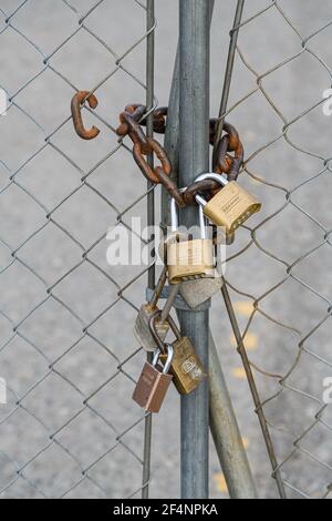 Multiple padlocks with a thick rusty chain on wire fence forbidding entry to the property behind Stock Photo
