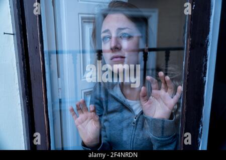 Young beautiful depressed unhappy caucasian woman looking worried and sad through the window at home. Feeling worthless and in pain. closeup. Depressi Stock Photo