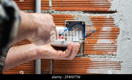 Electrician worker at work with a screwdriver fixes the cable in the terminal of the switch of a residential electrical system. Construction industry. Stock Photo
