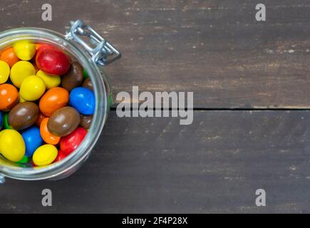 Colorful chocolate balls in glass jar in rustic wooden background.Top view with space for text. Stock Photo