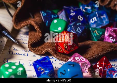 Close-up image of role playing dice of various shapes and colors spilling out of a leather dice bag on a open notebook. Stock Photo