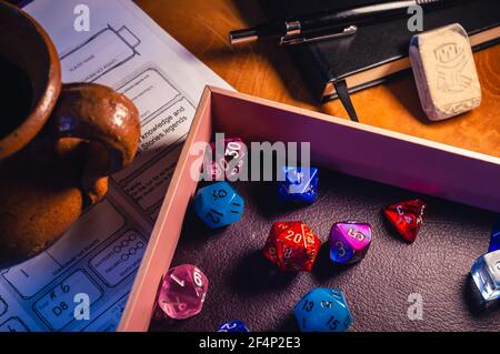 A close-up image of a pink dice tray filled with multicolor role playing dice, a ceramic drinking jar, a black notebook, a black pencil and an eraser Stock Photo