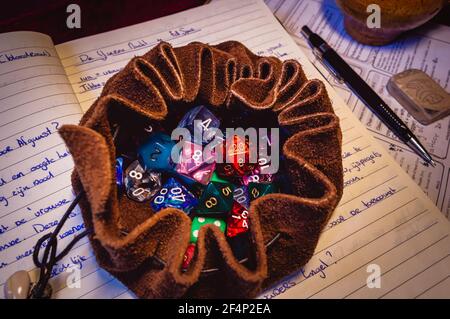 Close-up image of an open leather dice bag filled with multicolored roleplaying dice of various shapes on an open notebook, a black pencil and an eras Stock Photo