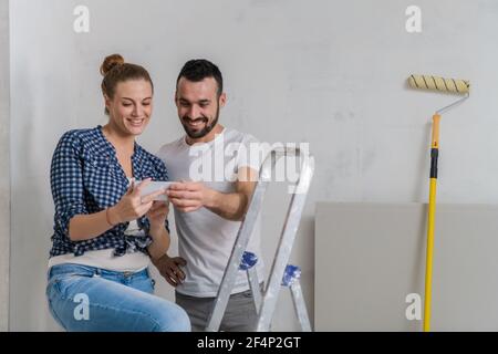 Man and woman sitting on a stepladder and looking at photos on the phone Stock Photo