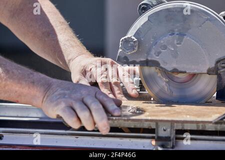 Close up of a man's hands using a wet tile saw to cut ceramic tile Stock Photo
