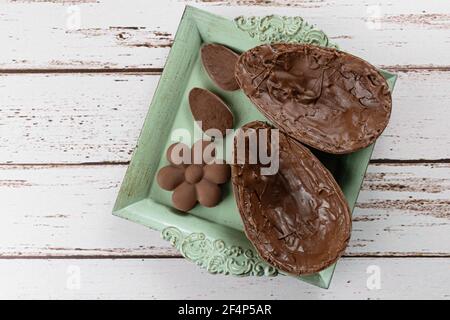Two halves of chocolate Easter egg, on a small old tray. Next to mini chocolates (top view). Stock Photo