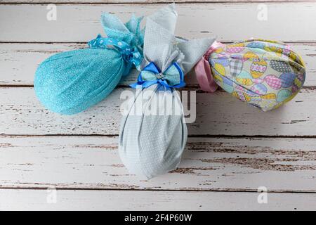 Chocolate Easter eggs packed with colorful fabrics and bows on a white wooden table. Stock Photo