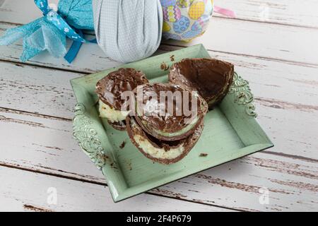 Two halves of chocolate Easter eggs filled with white brigadeiro and brigadeiro with pistachios. In the background, Easter eggs packed with colorful f Stock Photo