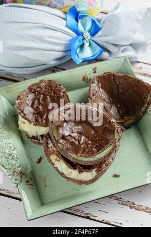 Two halves of chocolate Easter eggs filled with white brigadeiro and brigadeiro with pistachios. In the background, Easter eggs packed with colorful f Stock Photo