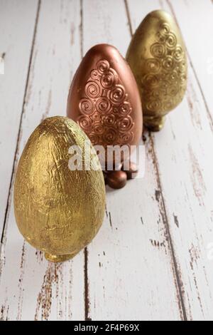 Three Easter eggs decorated with edible gold and copper paint. Lined up on a white wooden table. Stock Photo